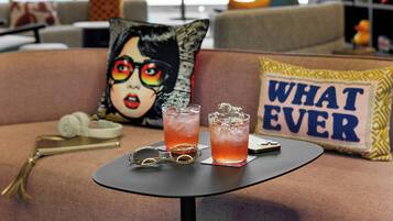 A table with two drinks, a pair of glasses, and a decorative pillow with the text "WHAT EVER" on a couch.