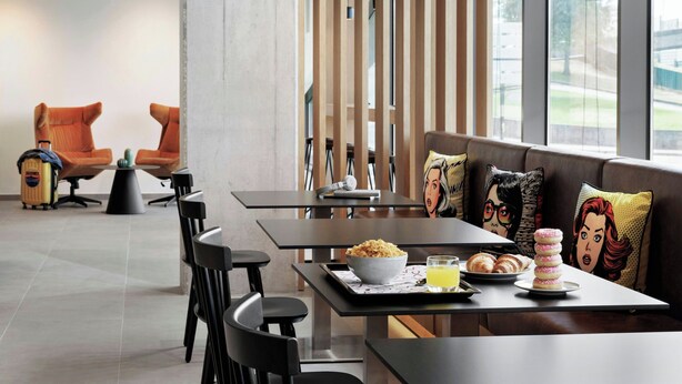 A modern dining area with tables, chairs, and a view of the outdoors. - Moxy Alfragide Lisboa (Amadora)