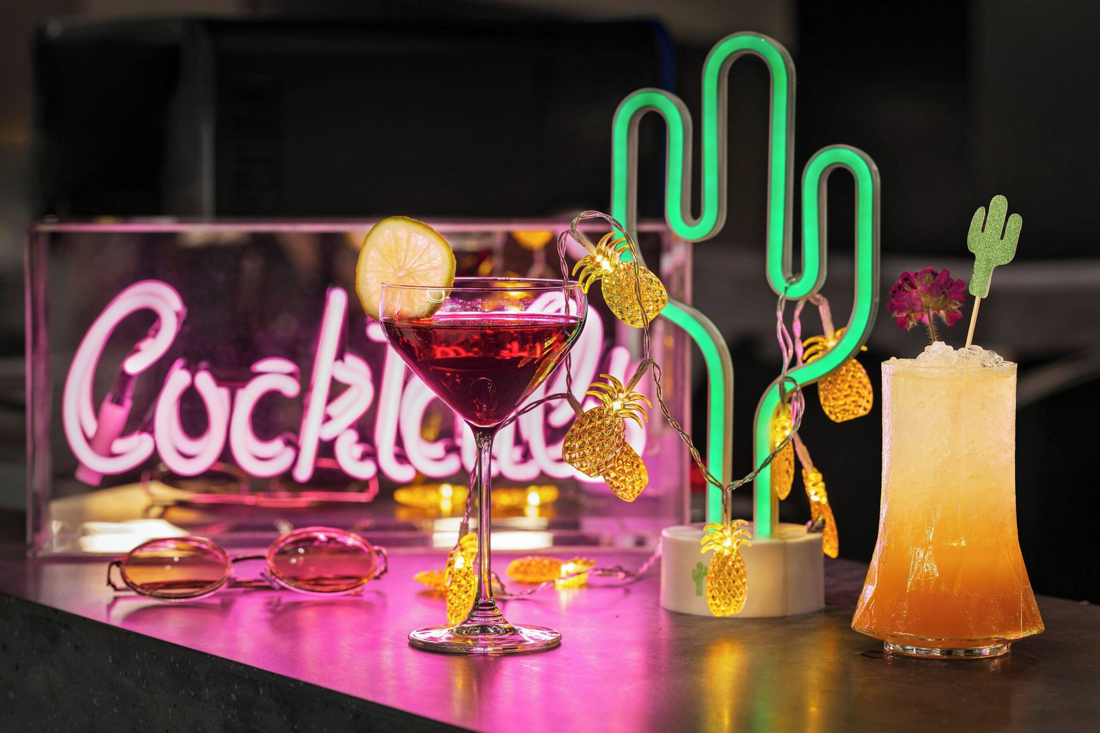 Een cocktailbar met een neonbord, een martini-glas, een highball-glas en decoratieve verlichting.