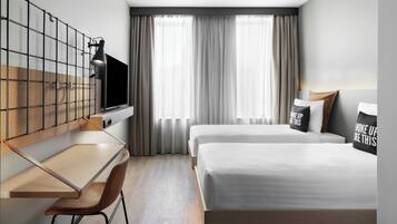 Una habitación de hotel moderna con escritorio, dos camas, televisor y un ventanal con cortinas.