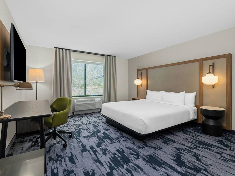 A hotel room with a bed, a desk, a chair, a television, and a window with curtains.
