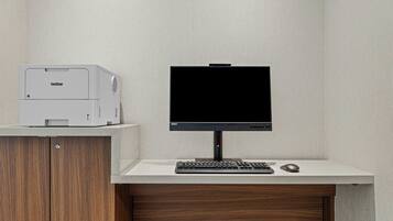 A modern office setup with a Brother printer, a flat-screen monitor, a keyboard, and a mouse on a white desk against a textured wall.