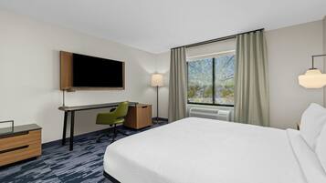 Een hotelkamer met een bed, bureau, stoel, televisie, lamp en raam met gordijnen.