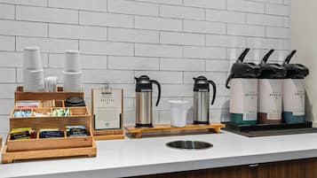 A coffee station with disposable cups, a coffee maker, and a coffee dispenser.