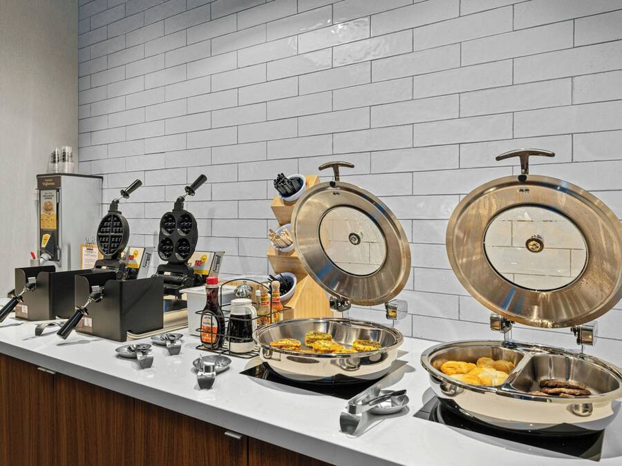 Un bufé de desayuno con planchas para gofres, máquinas de café y diversas opciones de comida.