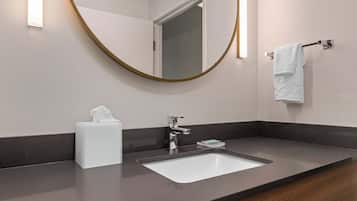 Un baño moderno con un lavabo blanco, grifo cromado y un espejo redondo con marco dorado.