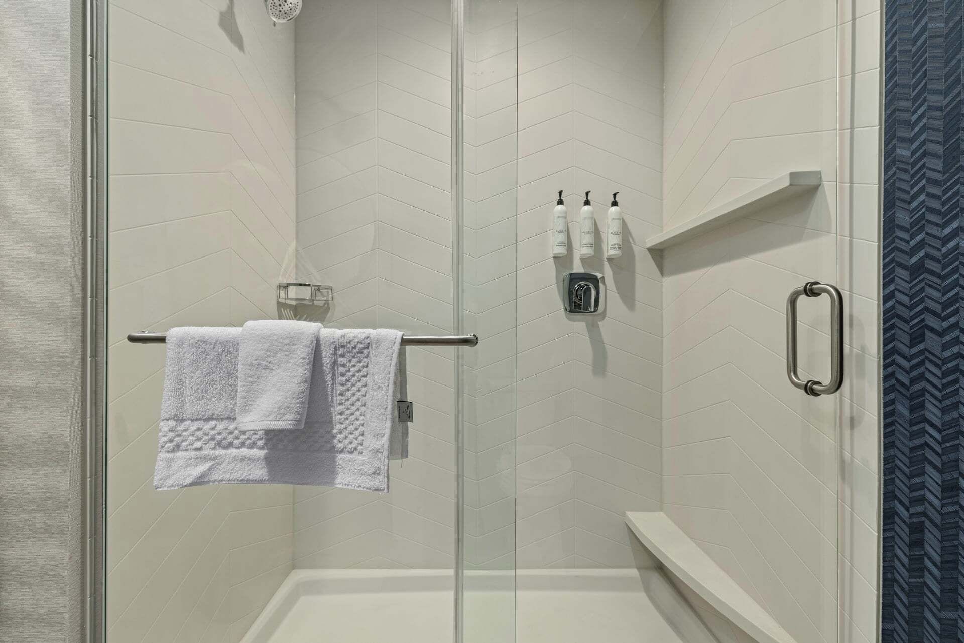Een douchecel met een glazen deur, een handdoekrek met een witte handdoek en toiletartikelen aan de muur.