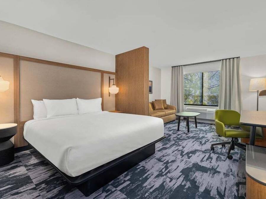 A hotel room with a large bed, a desk, a chair, and a sofa.