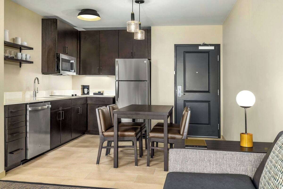 A modern kitchen with dark cabinets, stainless steel appliances, and a dining area with a table and chairs.