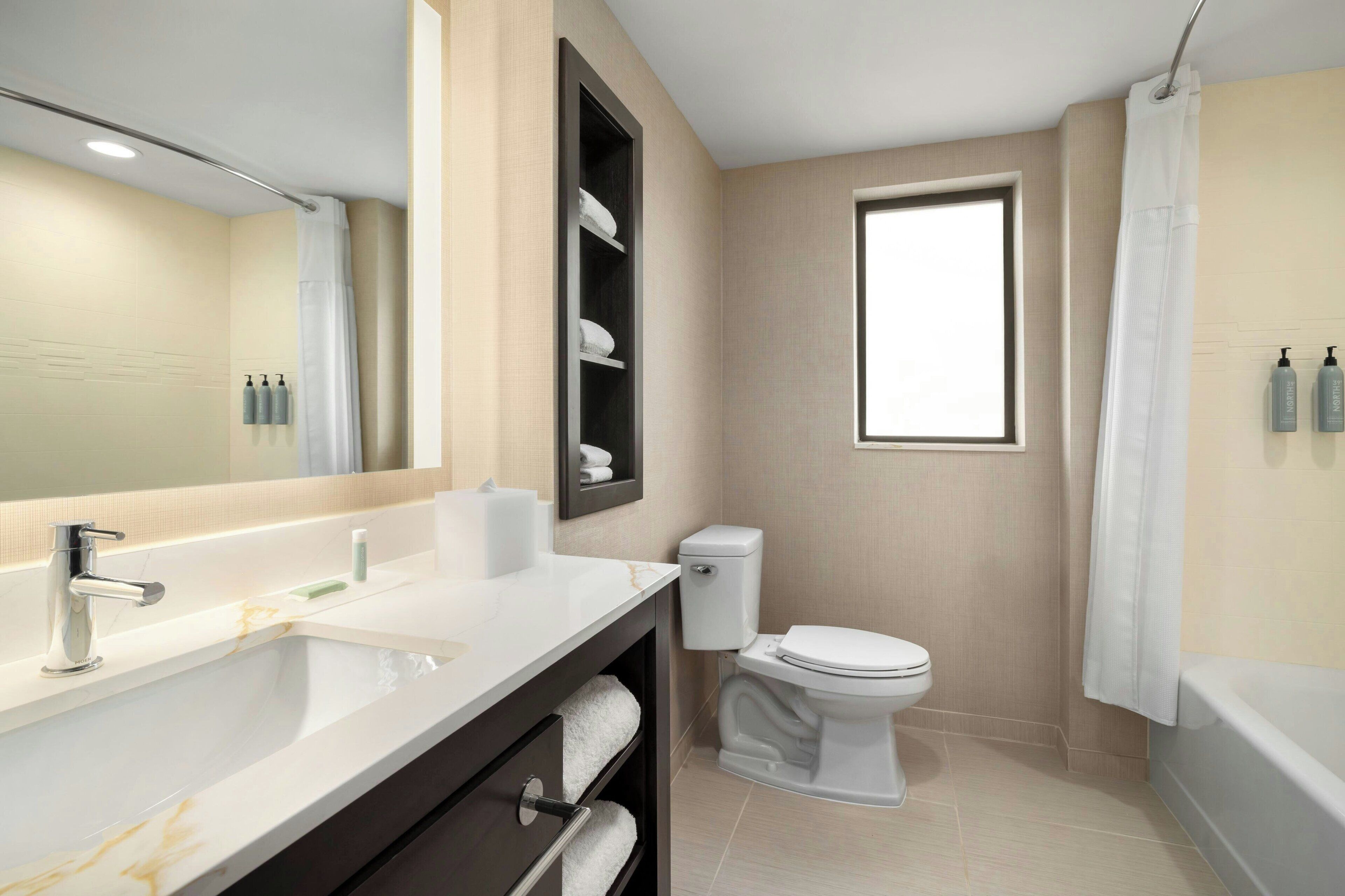 A modern bathroom with a large mirror, a white sink, a toilet, and a bathtub.