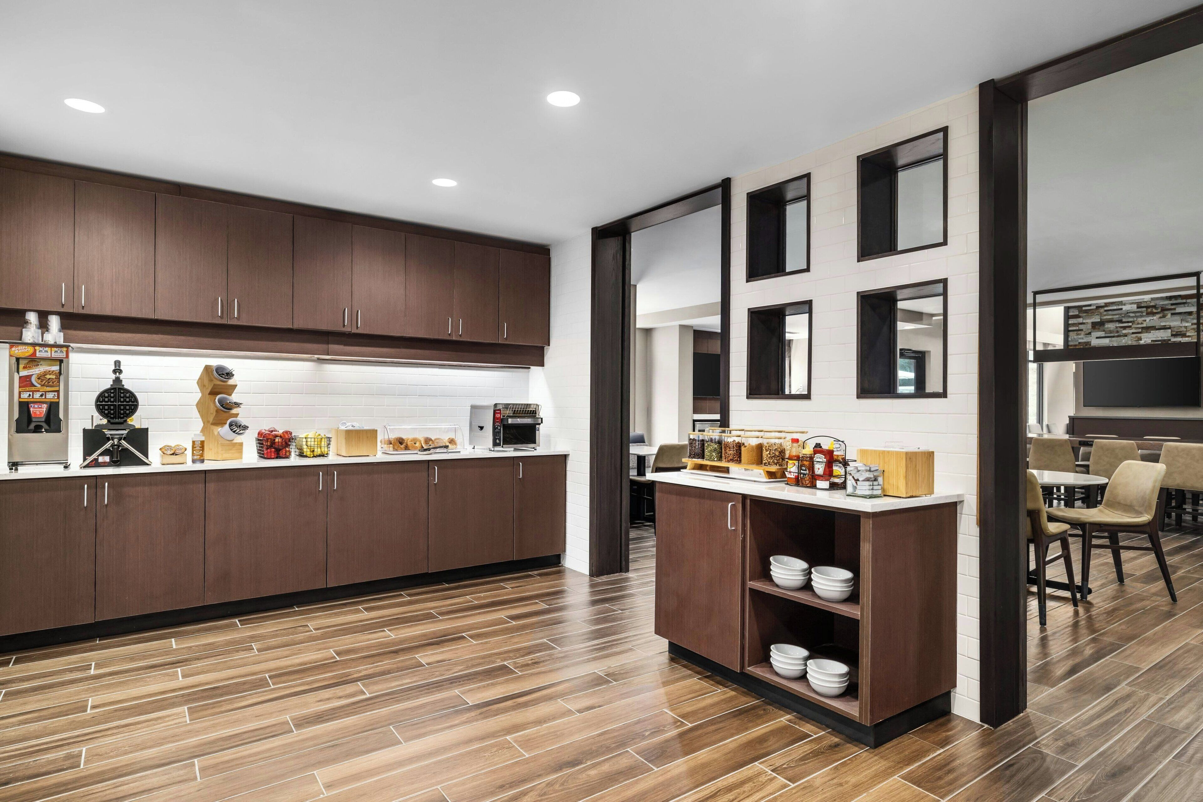 A modern kitchen with dark wooden cabinets, a white countertop, and a breakfast bar with bowls and condiments.