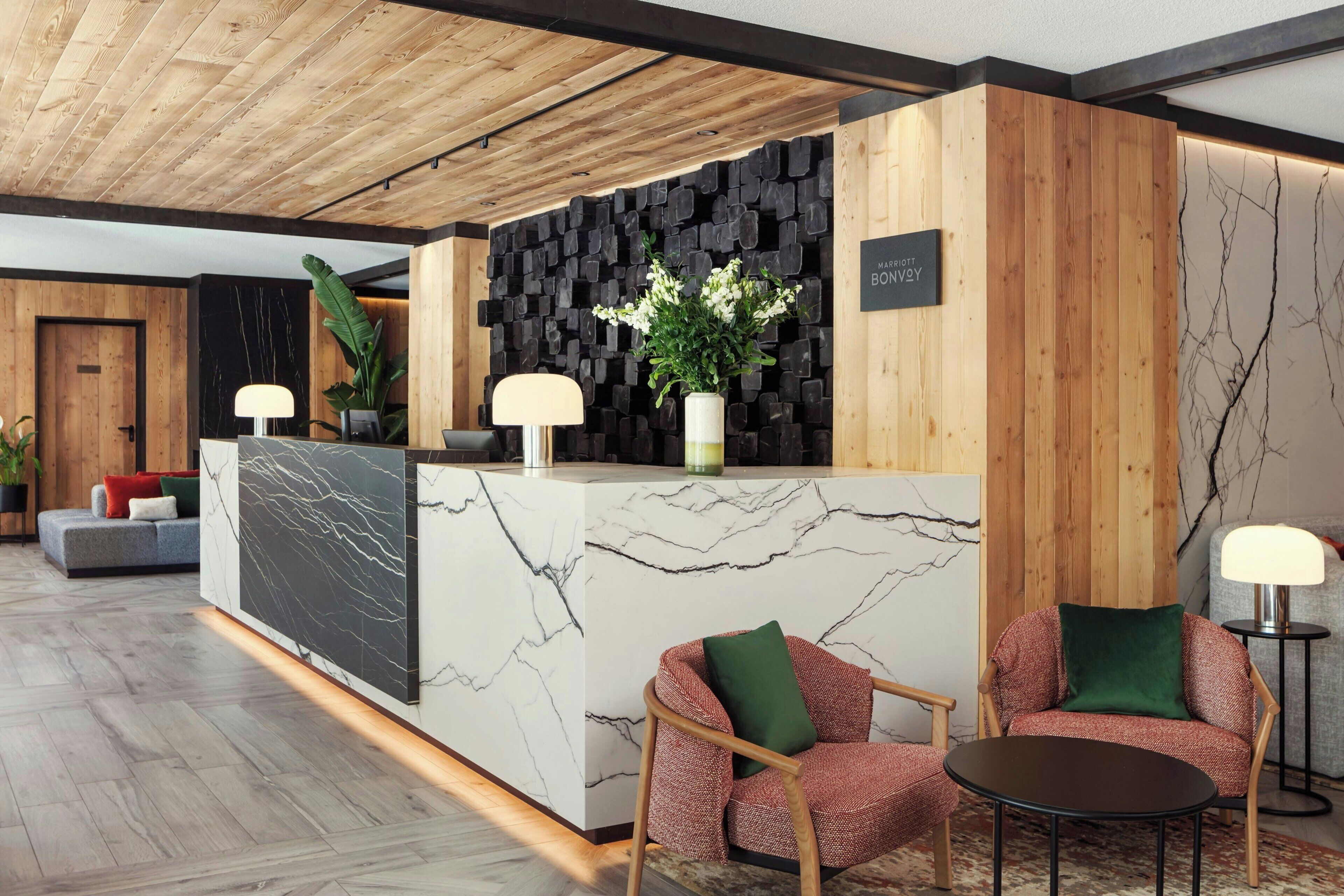 A reception desk with a marble top, wooden paneling, and a black wall with a plant. There are two chairs and a table in the foreground.