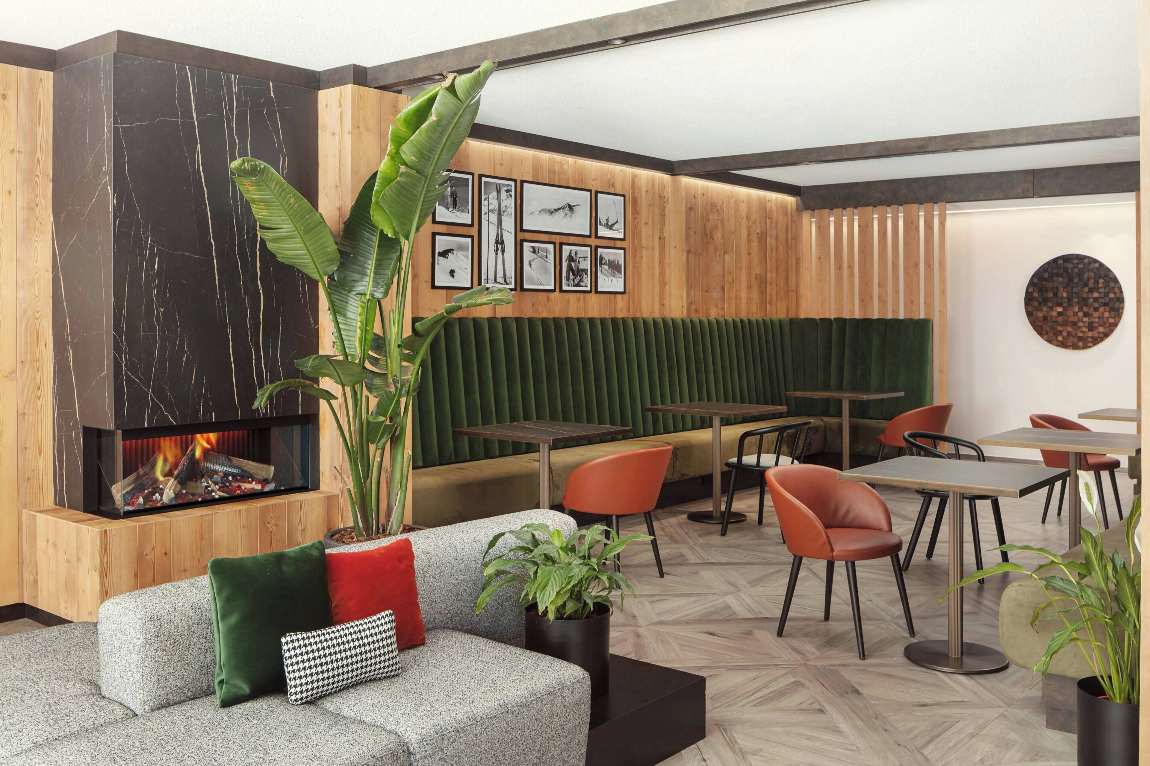Un interior moderno con chimenea, paneles de madera, asientos tapizados en verde y una pared de fotografías enmarcadas.