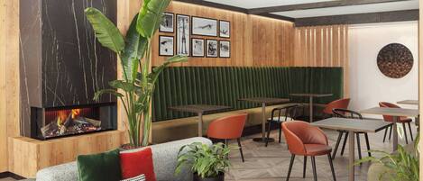 A modern interior with a fireplace, wooden panel walls, green upholstered seating, and a wall of framed photographs.