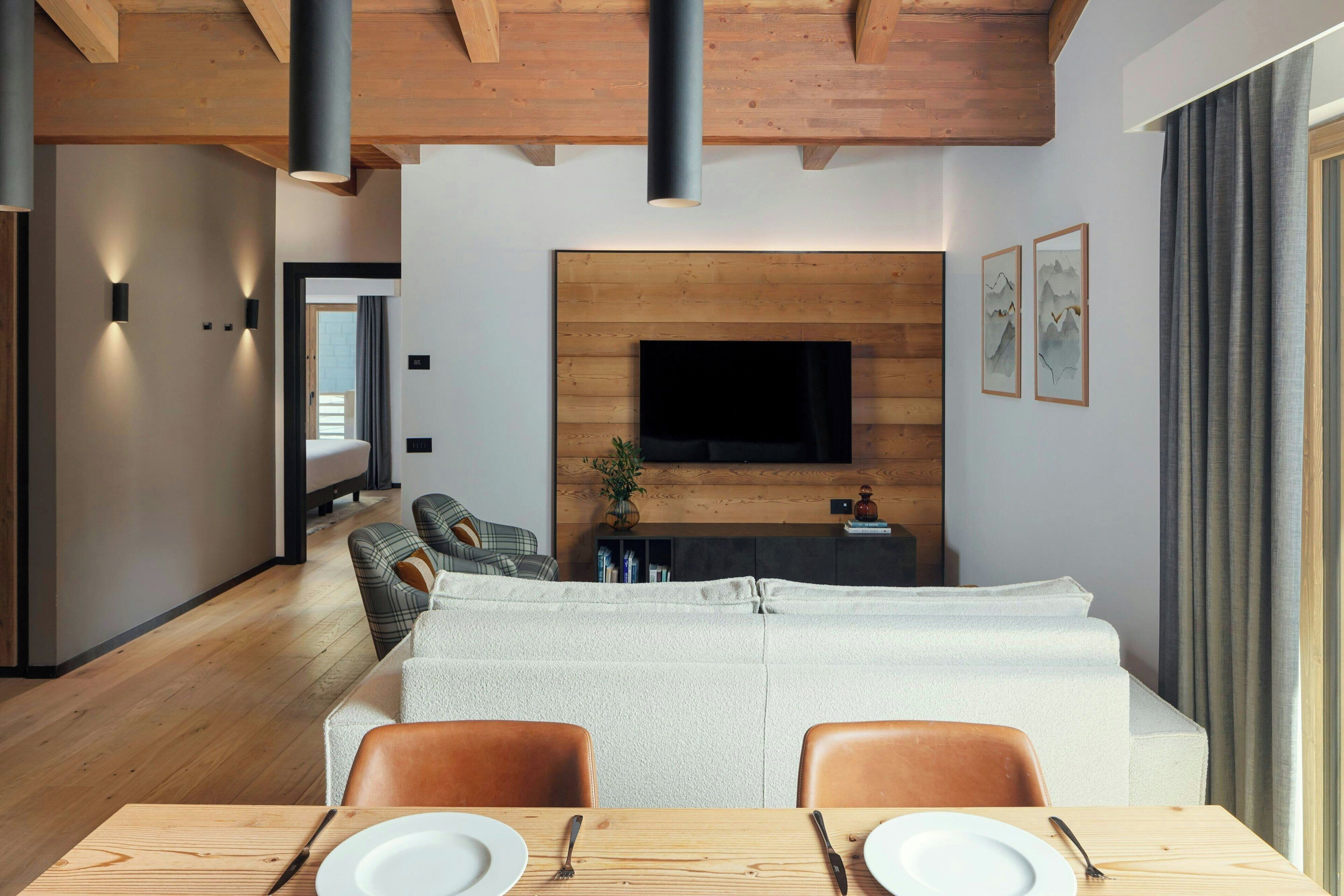 Una sala de estar moderna con un televisor de pantalla plana montado en una pared de madera, un sofá y un comedor con una mesa dispuesta para dos.