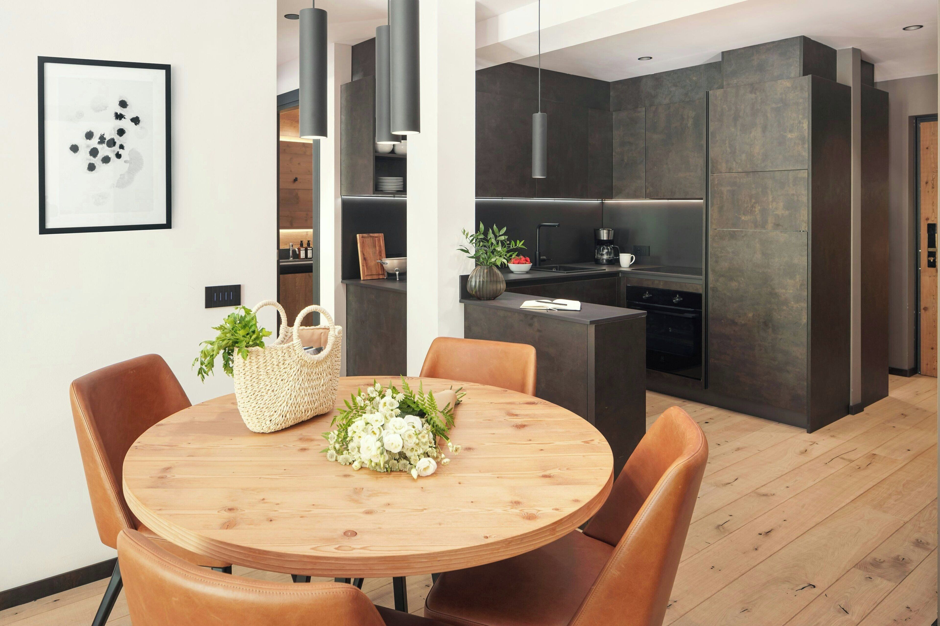 Una cocina moderna con armarios oscuros, una isla central y una zona de comedor con mesa de madera y sillas de cuero.
