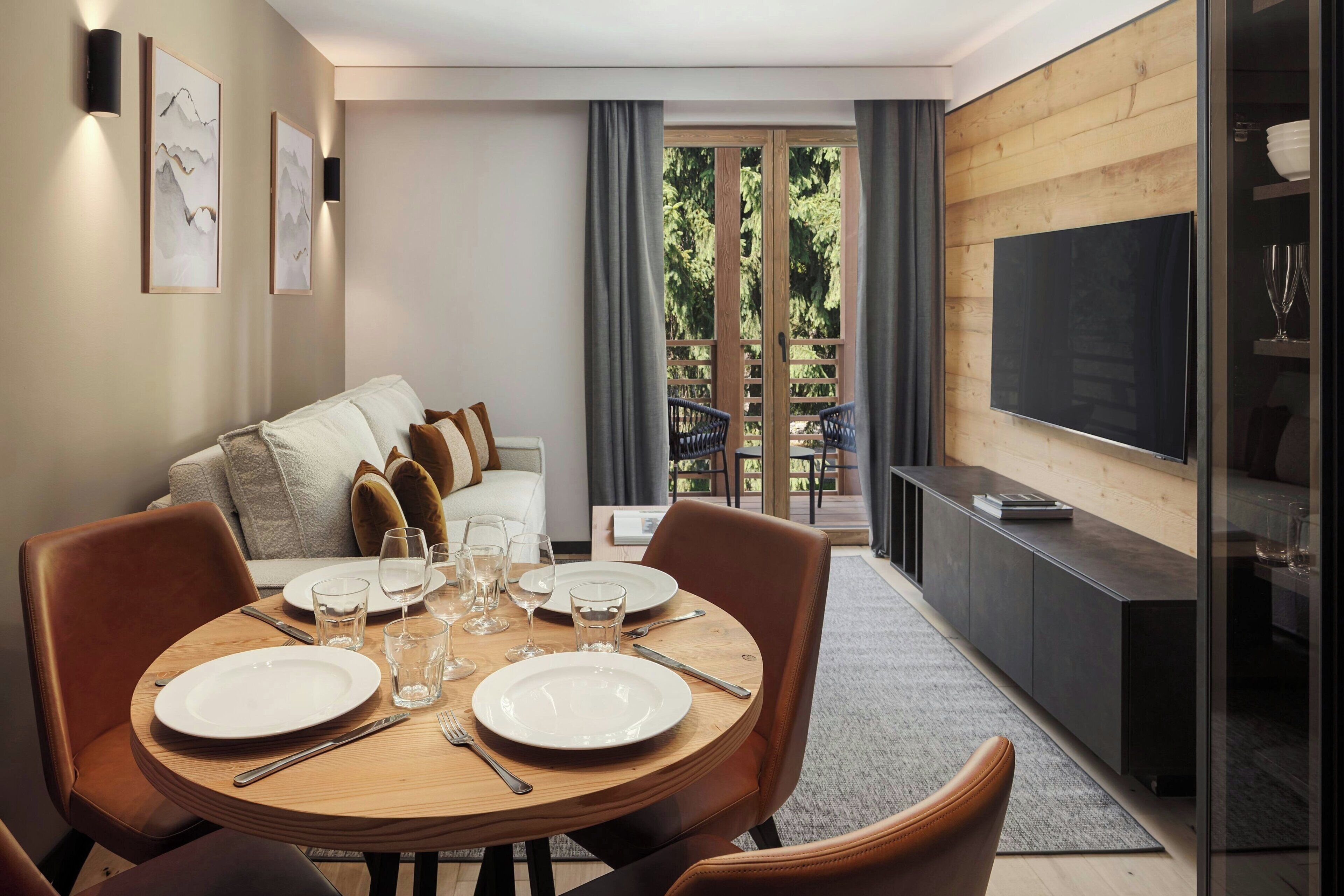 Een moderne woonkamer met een eethoek, een zithoek, een televisie en een balkon met uitzicht op bomen.