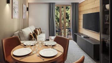 Een moderne woonkamer met een eethoek, een zithoek, een televisie en een balkon met uitzicht op bomen.