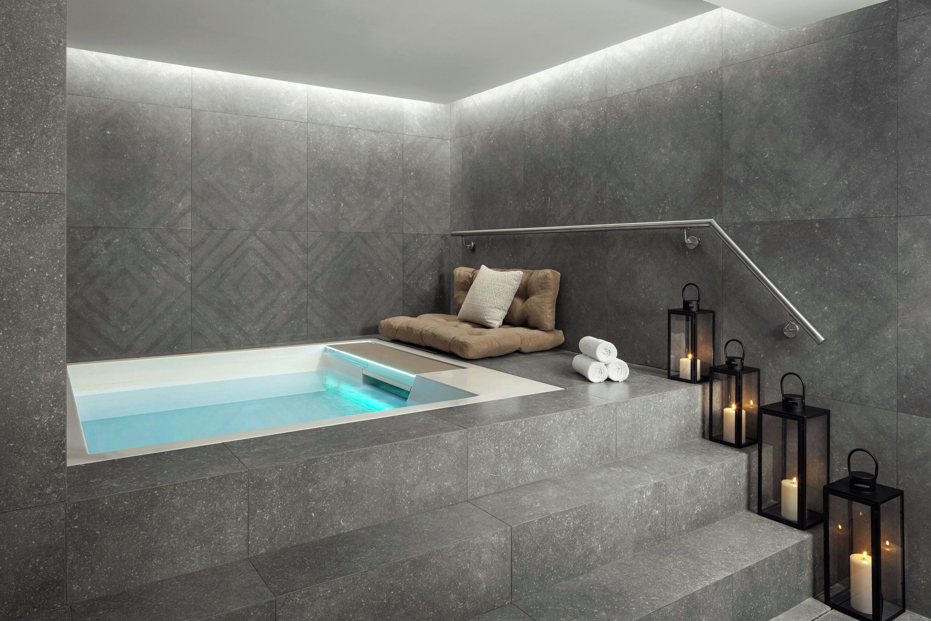 Een moderne badkamer met een ingebouwd bad, een zithoek met een kussen, en meerdere wandlampen.