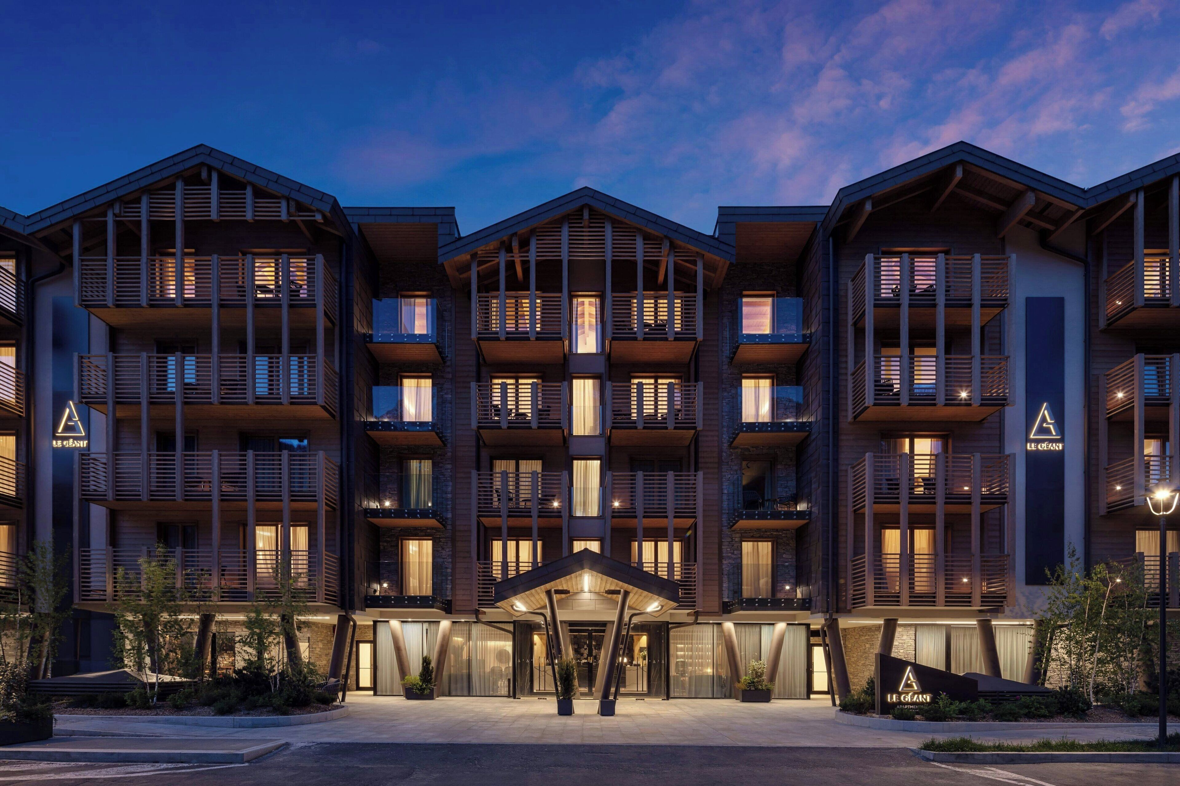 A multi-story hotel with balconies, a central entrance, and a landscaped area.