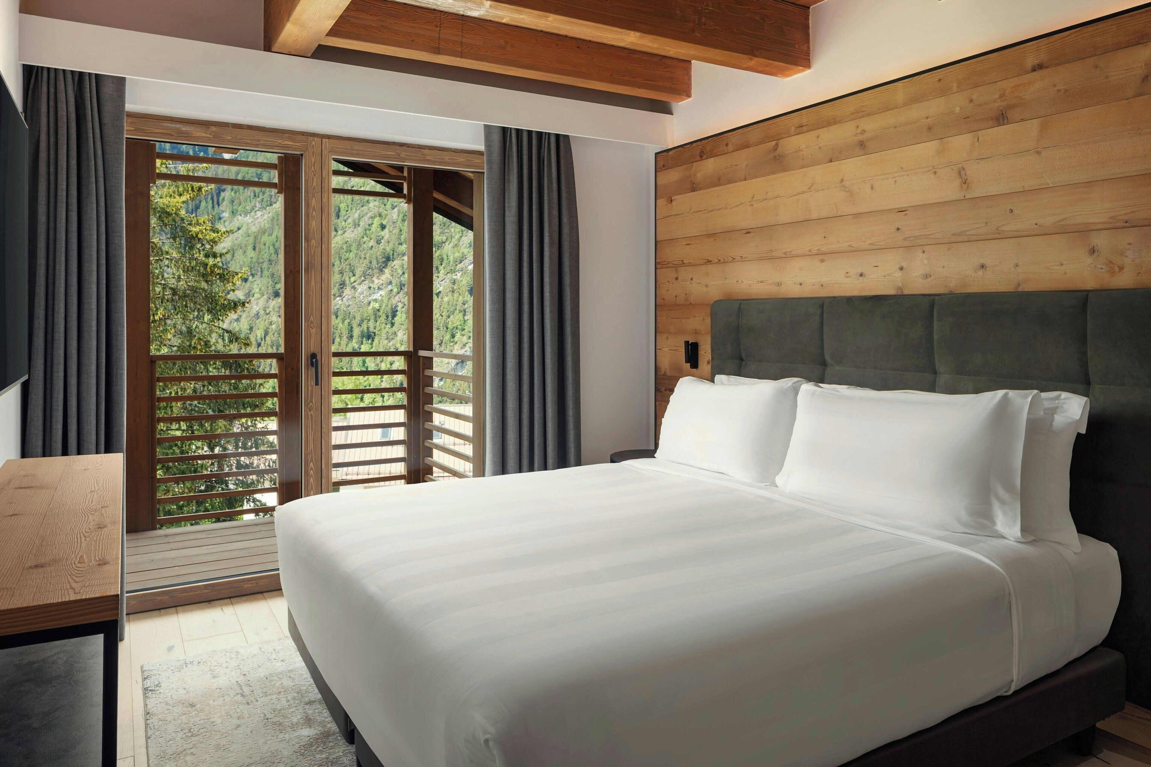 Ein Schlafzimmer mit einem großen Bett, einem Holz-Kopfteil und Blick durch eine Schiebetür in einen Außenbereich.