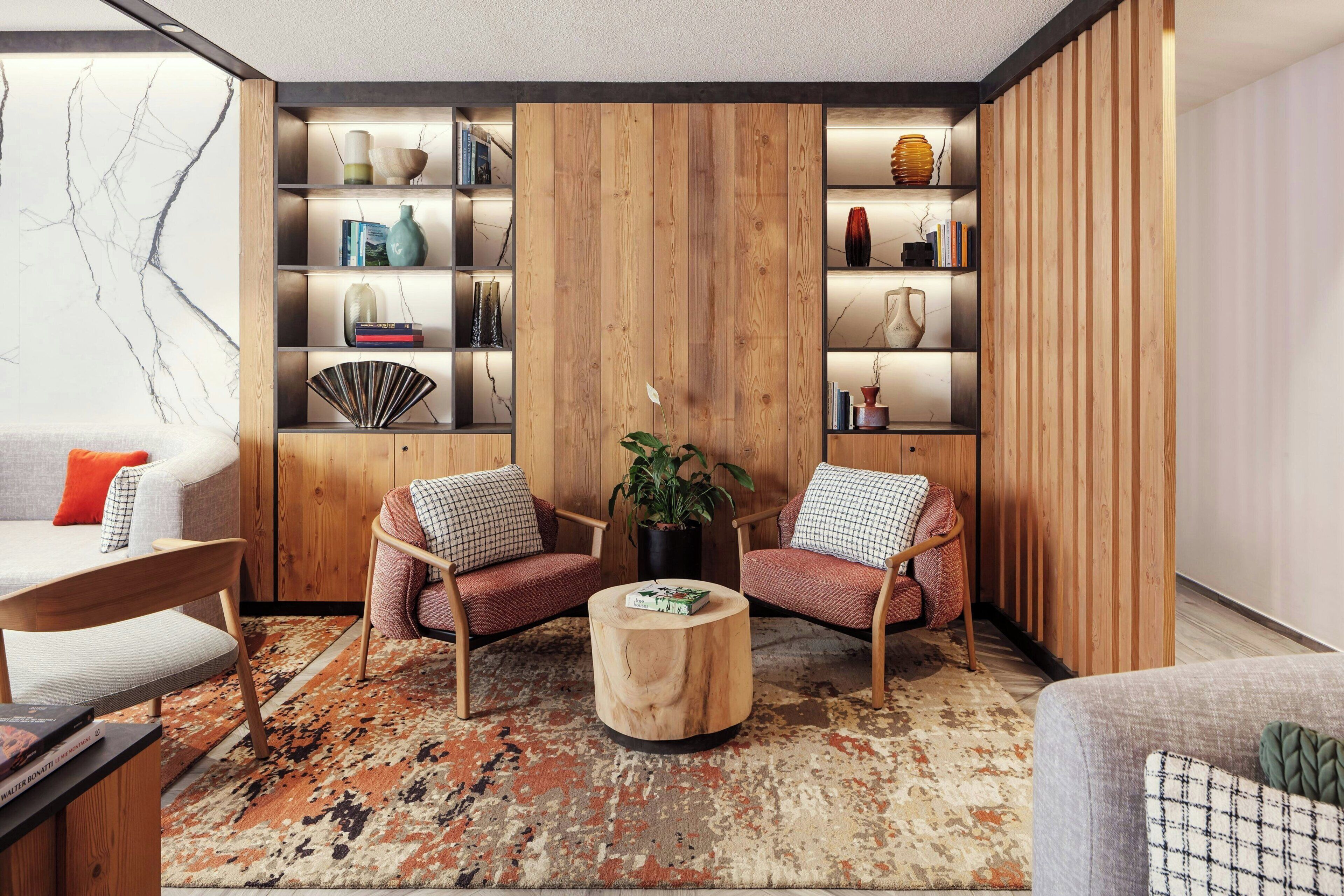 A modern living room with a wooden bookshelf, two armchairs, a round coffee table, and a patterned rug.