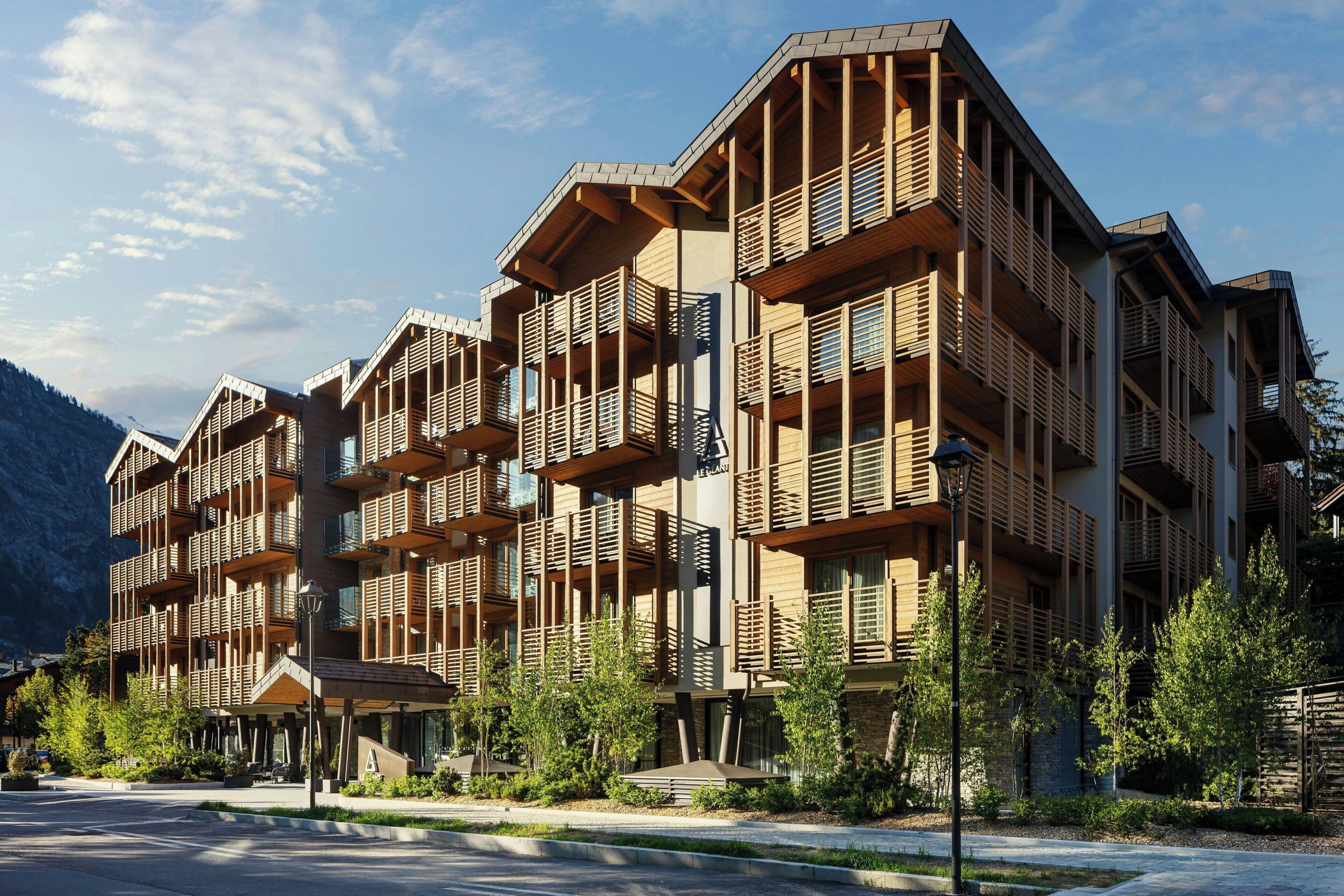 A multi-story hotel with balconies and a mountainous backdrop.