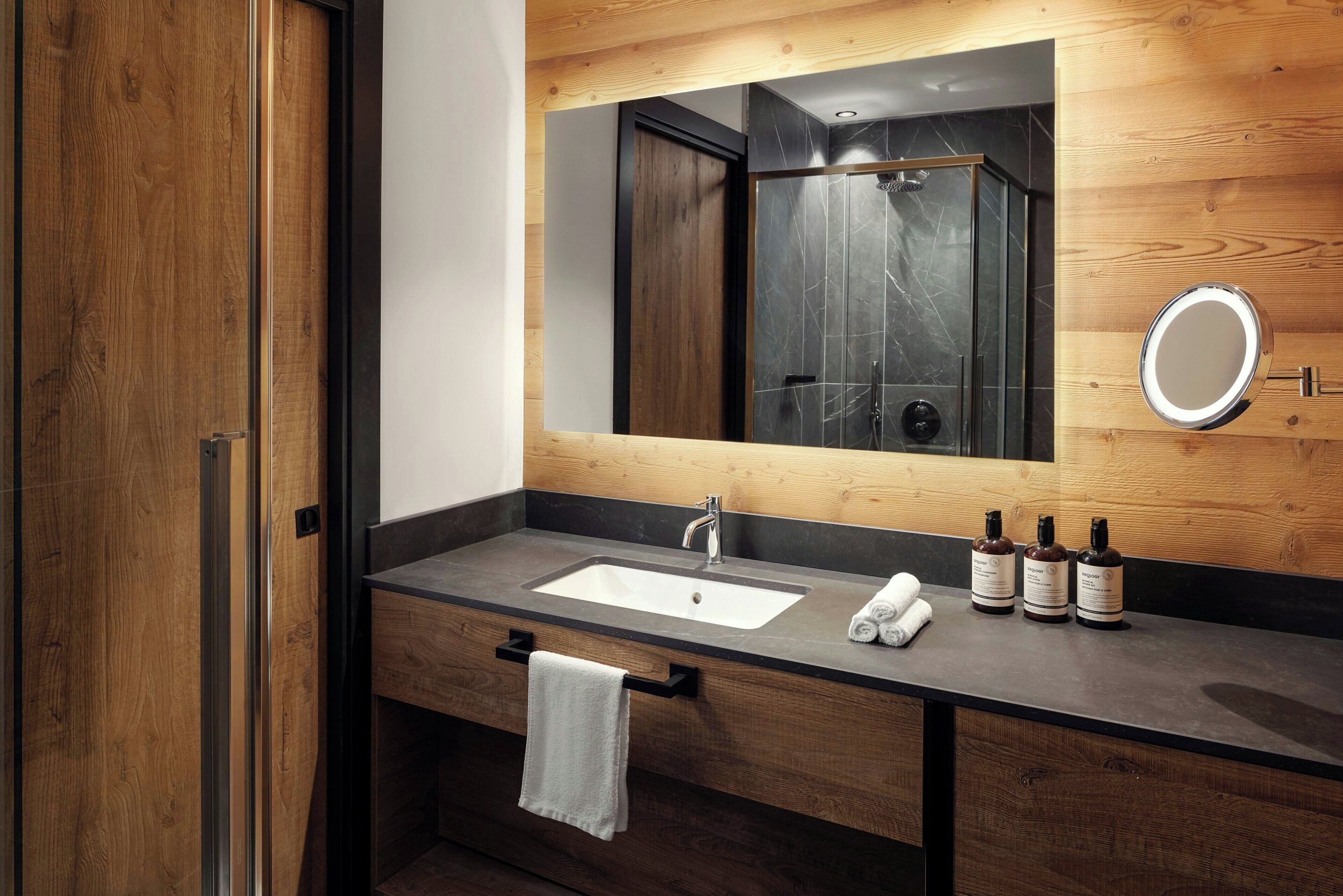 Un bagno moderno con un mobile bagno in legno, uno specchio grande, un lavandino e tre flaconi di shampoo.