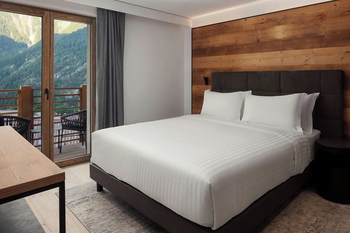 Ein Schlafzimmer mit einem großen Bett, einem Holzkopfende und Blick auf Berge durch eine Schiebetür.