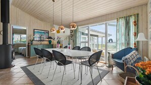 A spacious dining area with a large table and chairs, a kitchen in the background, and a view of the outdoors through large windows. - 3 bedroom lovely home in Knebel (Knebel)
