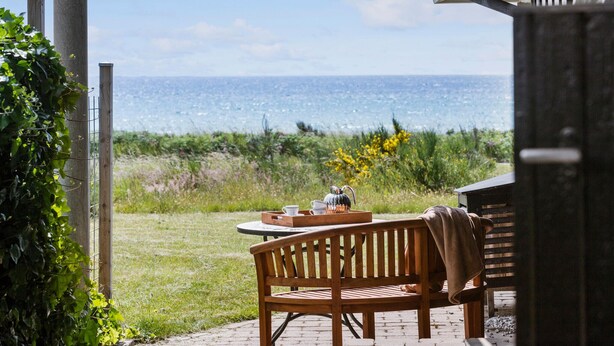 A wooden bench with a table and a kettle, overlooking a grassy area and the sea. - 3 bedroom lovely home in Knebel (Knebel)