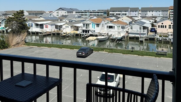 A view from a balcony overlooking a marina with several boats docked, a parking lot, and a row of houses along the water.