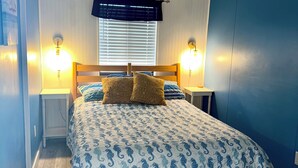 A bedroom with a wooden bed, patterned bedding, two bedside lamps, a window with blinds, and a nightstand.