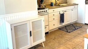 A kitchen with white cabinets, a stove, and a microwave. There is a sign on the wall and a small plant on the counter.