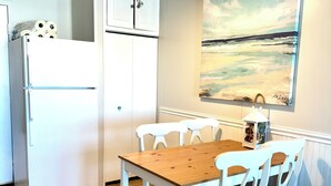 A compact kitchen with white cabinets, a refrigerator, a wooden table, and white chairs.