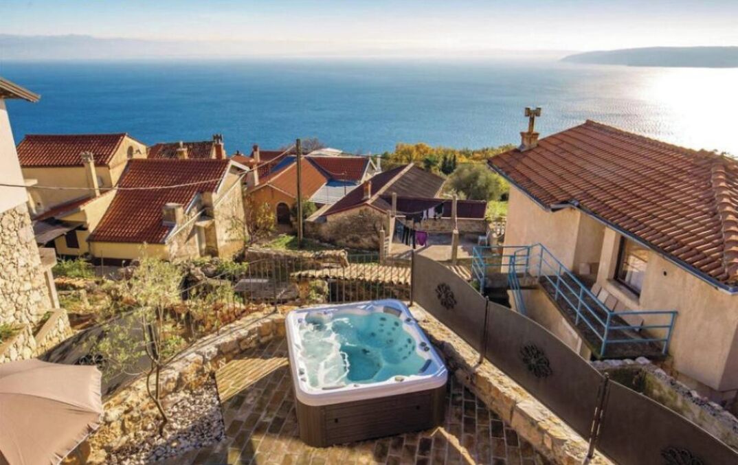 A hot tub surrounded by stone walls and terraced houses with a view of the sea.