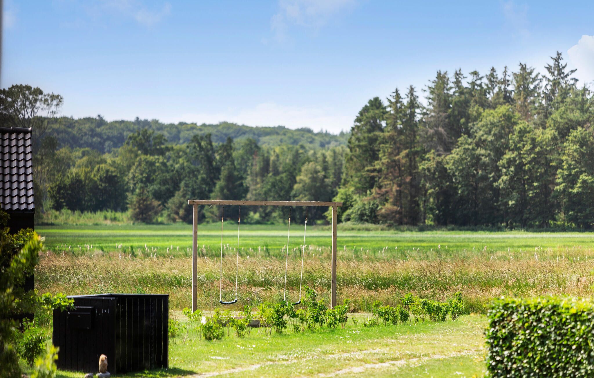 A rural landscape with a wooden swing set in a field, surrounded by trees and a clear sky.