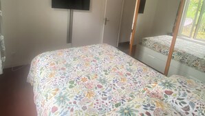 A bedroom with a floral bedspread, a television mounted on the wall, and a large mirror reflecting the bed and window. - Quiet house in Vernon (Vernon)