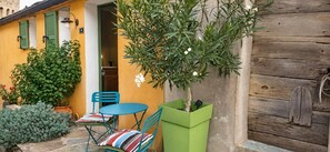 Ein Außenbereich mit Sitzgelegenheit, Tisch, Stühlen, einem Blumentopf und einer Holztür.