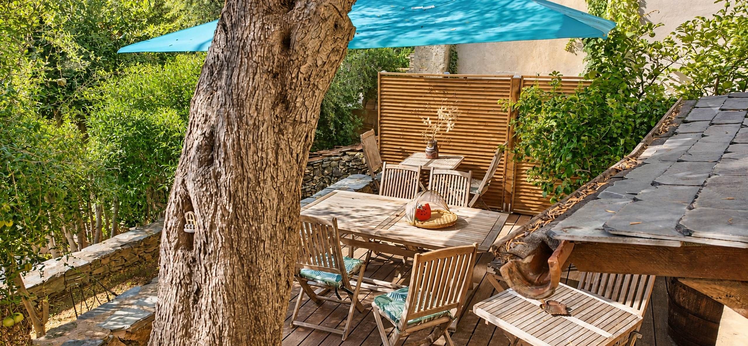 Un patio exterior con mesa y sillas, una valla de madera y un árbol.