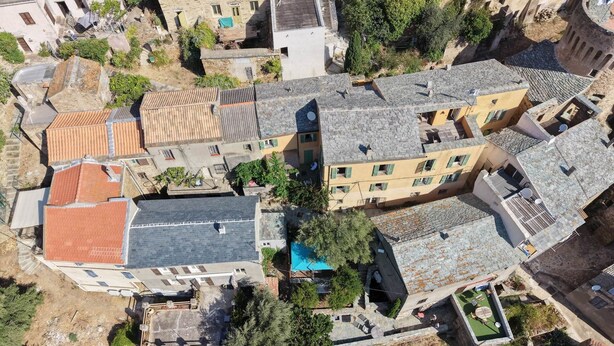 An aerial view of a residential area with stone buildings, a swimming pool, and surrounding greenery. - LATU CORSU – Cosy studio for 2 (ERSA)