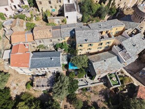 An aerial view of a residential area with stone buildings, a swimming pool, and surrounding greenery.