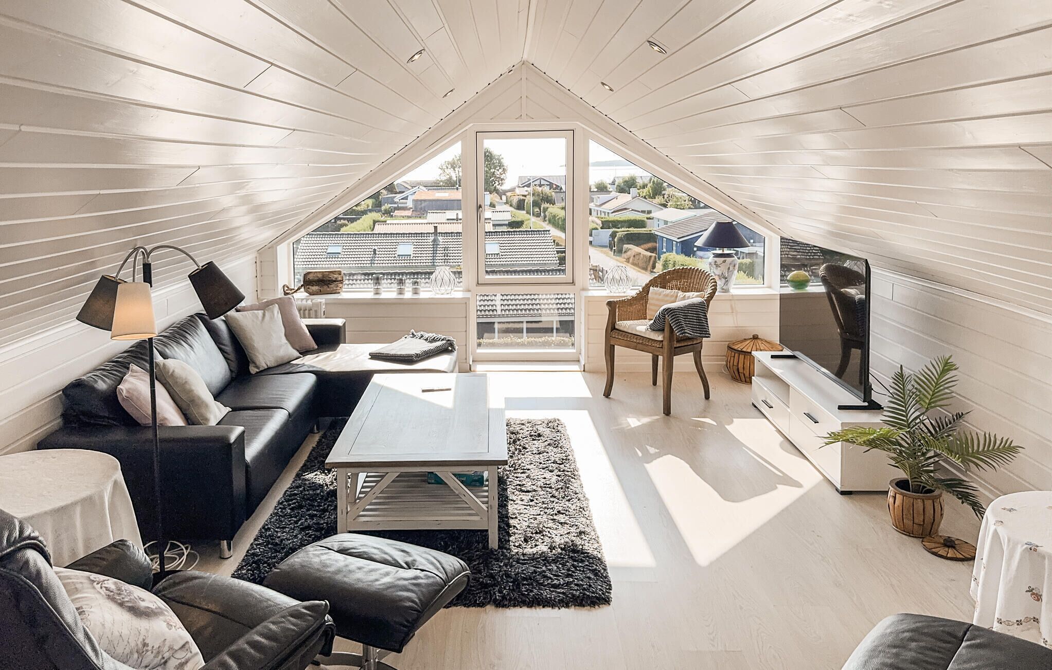 Una sala de estar moderna tipo loft con un ventanal grande, un sofá, una mesa de centro, un televisor y una planta en maceta.