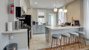 A modern kitchen with a central island, bar stools, and a fire extinguisher. - SunSuite - 6 Min. Walk to Trains - Summer Special! (Jersey City)