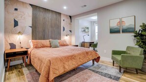 A bedroom with a large bed, bedside tables, a green armchair, and artwork on the wall. - SunSuite - 6 Min. Walk to Trains - Summer Special! (Jersey City)
