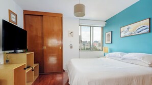 Een slaapkamer met een bed, een houten garderobe, een televisie en kunst aan de muur.