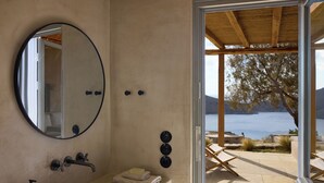 A bathroom with a bathtub, a round mirror, and a view of a lake through an open door. - Mousti's Cell Traditional Cycladic Farmhouse (Serifos Island)
