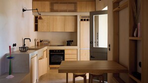 A compact kitchen with wooden cabinets, a built-in oven, and a dining area with a table and chairs. - Mousti's Cell Traditional Cycladic Farmhouse (Serifos Island)