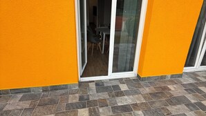 A building with a bright orange exterior, a sliding glass door leading to an indoor space with a table and chairs, and a tiled patio area.