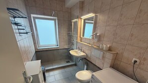 A modern bathroom with a window, a sink, a toilet, and a washing machine.